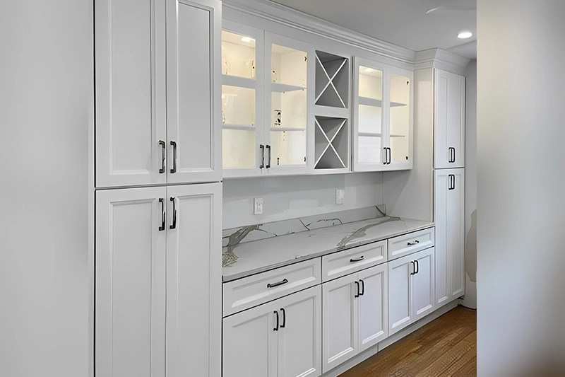 A modern white kitchen with marble countertops and built-in cabinets.