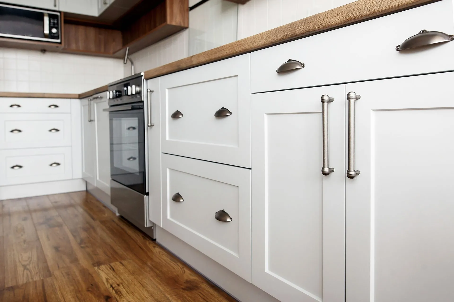 Close-up of white kitchen cabinets with silver handles and wooden floor.