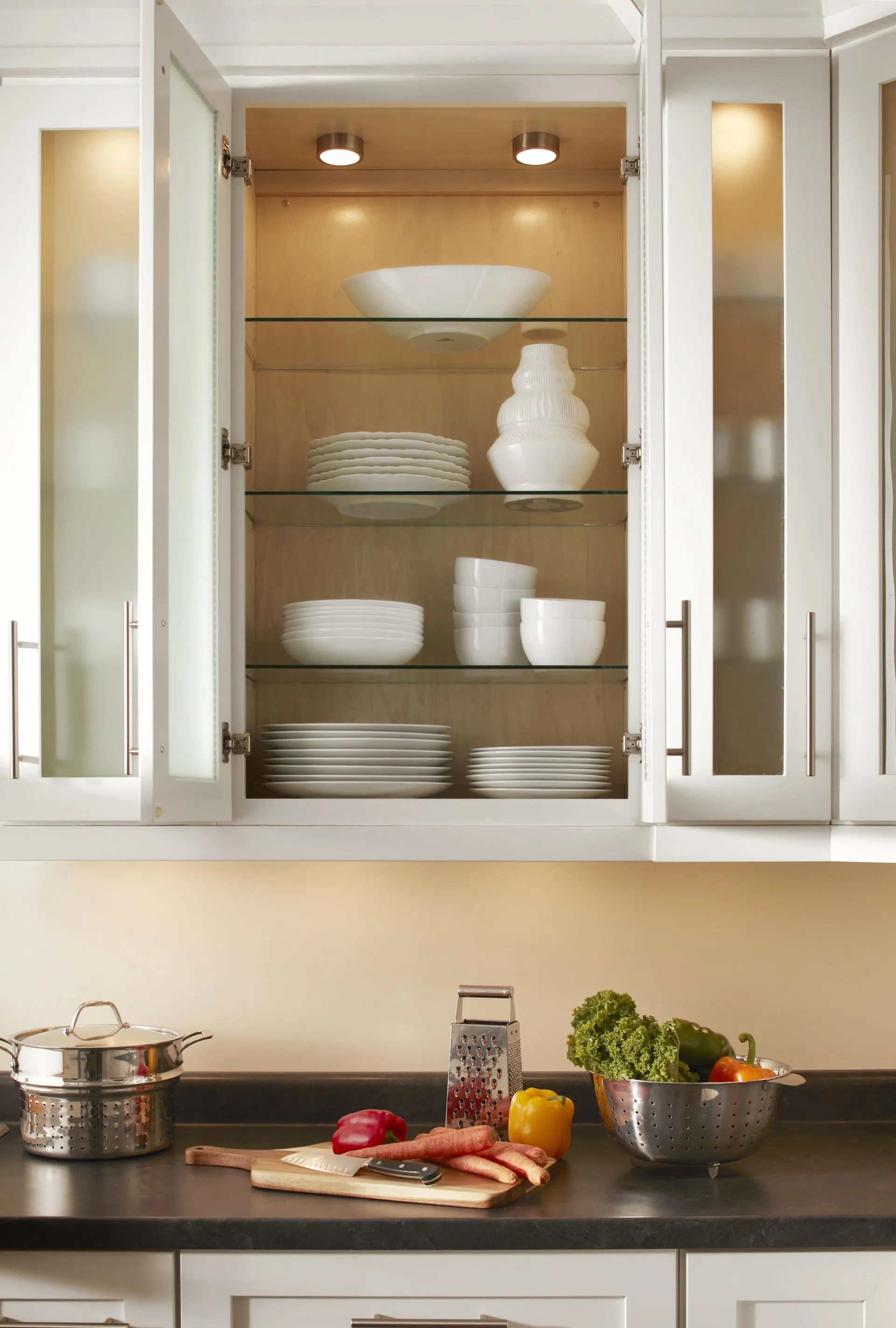 A kitchen cabinet with glass doors displaying white dishes and bowls.